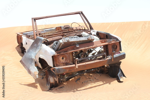 Burnt out wreckage of a SUV (4-wheel-drive) vehicle rusts away in hot and arid desert sand dunes terrain in Sharjah emirate in the United Arab Emirates.  