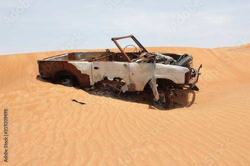 Burnt out wreckage of a SUV (4-wheel-drive) vehicle rusts away in hot and arid desert sand dunes terrain in Sharjah emirate in the United Arab Emirates.  