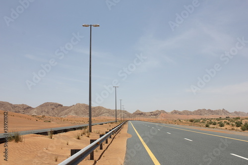 Modern asphalt highway passes through arid desert sand dunes terrain in Sharjah emirate in the United Arab Emirates.  