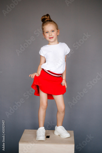 young little girl in red skirt having fun in studio with gray background. Studio portrait of young funny girl. White blonde little stylish fashion woman. Smiling child. yoth juvenile  photo