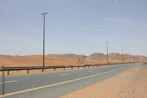 Modern asphalt highway passes through arid desert sand dunes terrain in Sharjah emirate in the United Arab Emirates.  