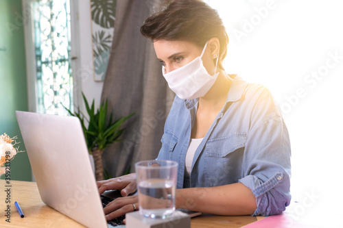 a woman wearing a surgical mask and teleworking at home