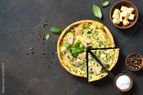 Quiche (pie) with salmon, spinach and soft cheese on a dark concrete background. View from above. photo