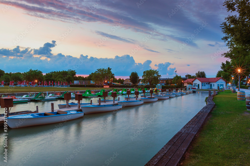 View of the mooring of small boats in the town of Podersdorf on Lake Neusiedl in Austria. In the background is a dramatic sunset sky.