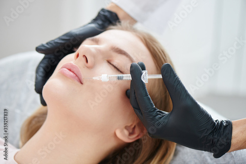 Beautician doctor injects hyaluronic acid on the lips of a young beautiful woman in a beauty salon. Lip augmentation close up