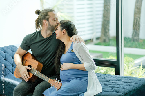 Schilderij op canvas Man hold guitar and kiss on his pregnant wife forehead to express love and care in family