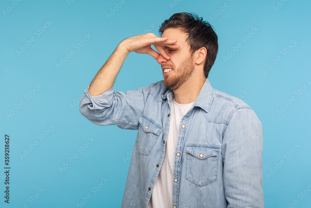 Awful stink! Portrait of man in worker denim shirt grimacing in disgust, pinching nose to avoid bad smell, fart gases, expressing repulsive emotions. indoor studio shot isolated on blue background Awful stink! Portrait of man in worker denim shirt grimacing in disgust, pinching nose to avoid bad smell, fart gases, expressing repulsive emotions. indoor studio shot isolated on blue background
