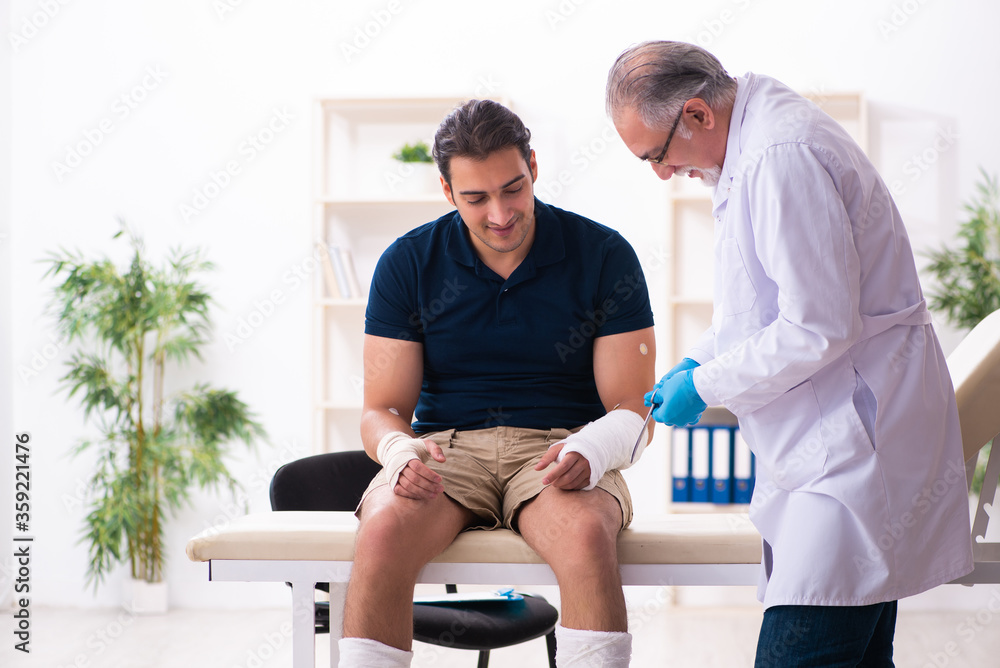 Fototapeta premium Young injured man visiting old doctor traumatologist