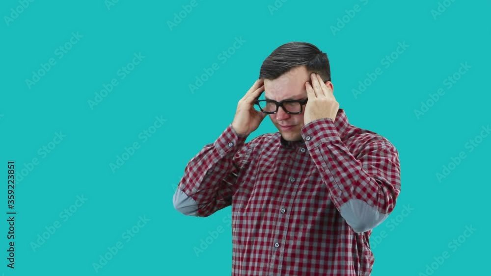 A man dressed in a plaid shirt and glasses holds his hand to his head from a headache, stands sideways. A man dressed in a plaid shirt and glasses holds his hand to his head from a headache, stands sideways.