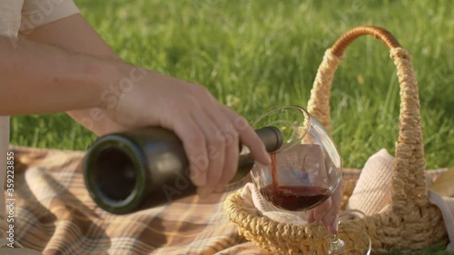 Close up male hand pouring wine into a wineglass. People enjoing outdoor picnic in nature. Summer day in the park. Relaxing and recreation concept