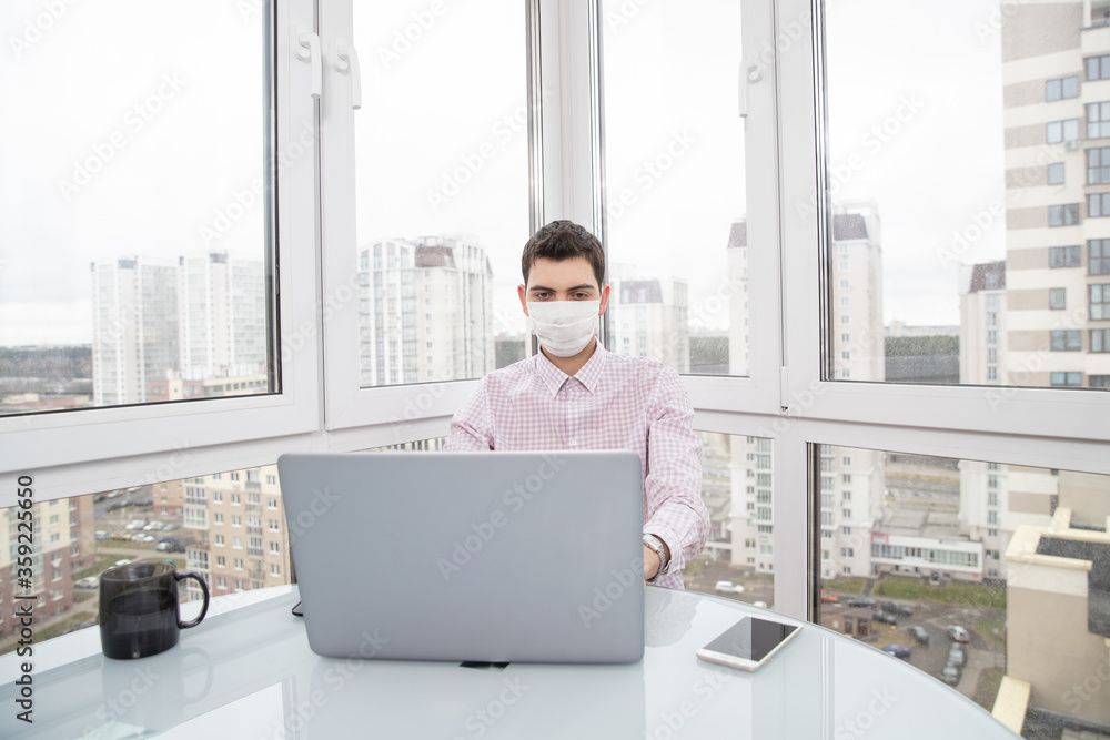 A guy in a protective face mask works at a computer from home during a virus epidemic. Quarantine during viral infection A guy in a protective face mask works at a computer from home during a virus epidemic. Quarantine during viral infection