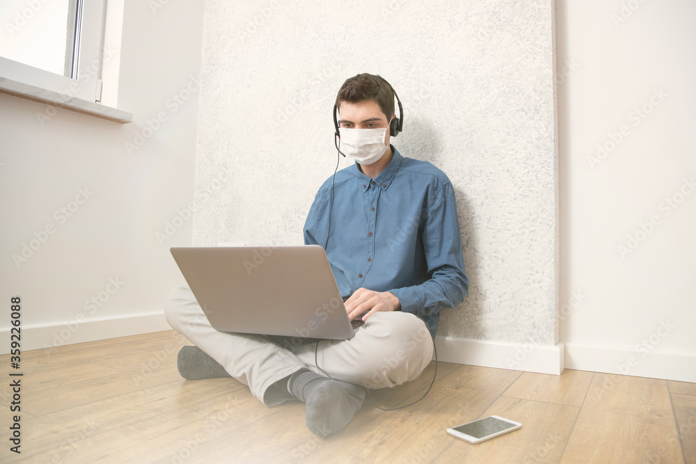 A guy in a protective face mask is working at a computer in an empty room at home during a virus epidemic. Quarantine during viral infection A guy in a protective face mask is working at a computer in an empty room at home during a virus epidemic. Quarantine during viral infection