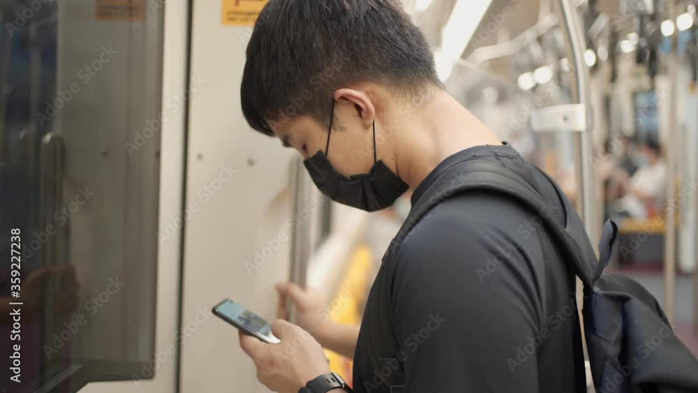 Asian man Wear black mask standing inside sky train head down scrolling phone, Commuter on rail ride, covid-19 new normal, risk on public transport, social distance, smartphone user on the train Asian man Wear black mask standing inside sky train head down scrolling phone, Commuter on rail ride, covid-19 new normal, risk on public transport, social distance, smartphone user on the train