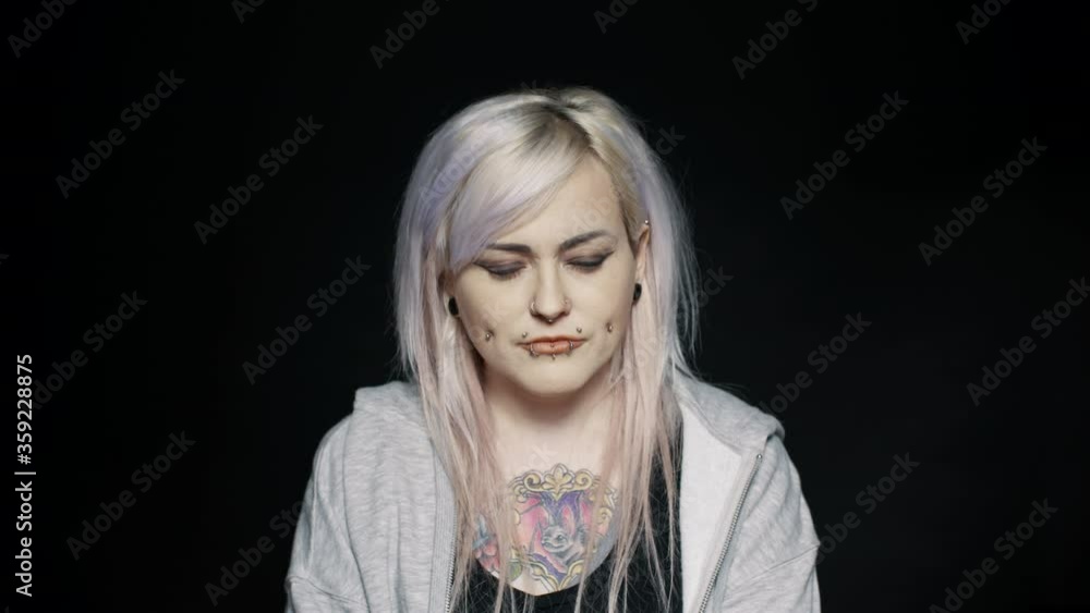 Close up of woman with white hair and tattoo on body with her eyes closed. Woman with fashion piercing on lips and cheeks on black background.
Close up of woman with white hair and tattoo on body with her eyes closed. Woman with fashion piercing on lips and cheeks on black background.
