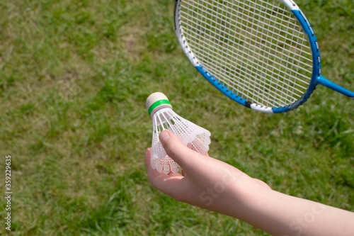 Badminton game with a shuttlecock on the nature. Child holds shuttlrcock on green grass background