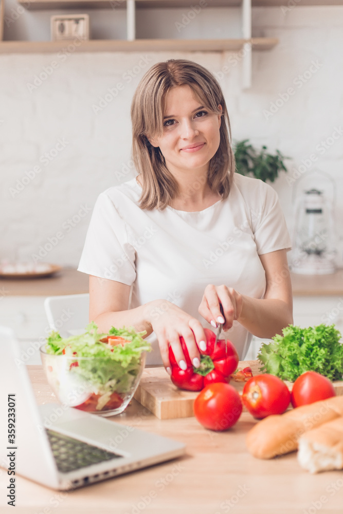 Woman cutting vegetables on salad and view recipes in laptop on kitchen. Woman cutting vegetables on salad and view recipes in laptop on kitchen.