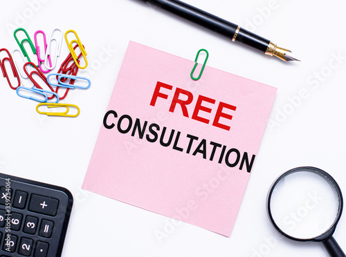Free consultation is written in a notebook that lies on a white table with a pen, magnifying glass , colored paper clips and a calculator. Business concept.