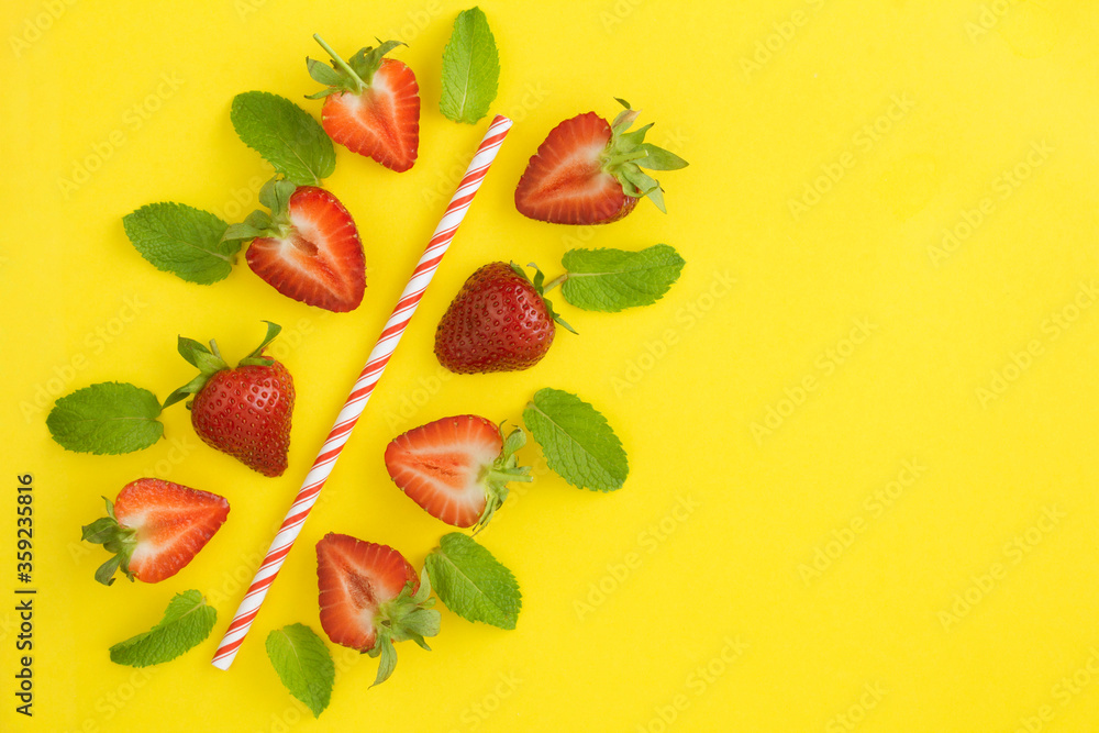 Composition with a cocktail straw, strawberries and mint  on the yellow background. Top view. Copy space.