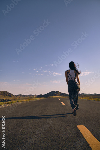 Asian girl walking along the road in between mountains.