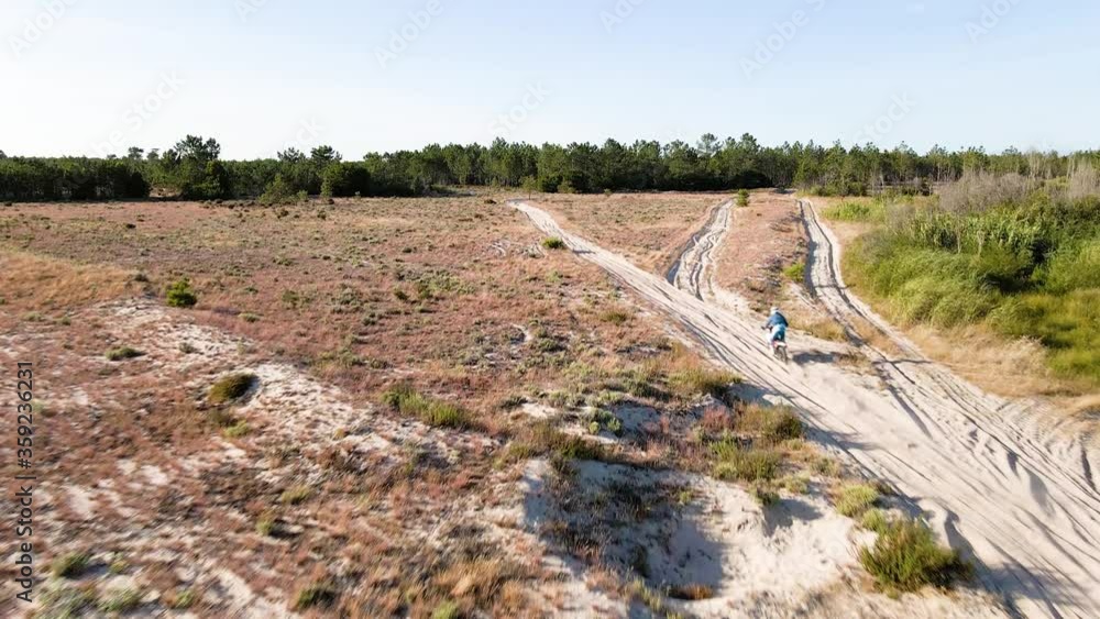 Aerial drone shot view of one enduro motorcycle drive through path or sandy trail on pine trees field during off road training in countryside. Adrenaline rush fun. Aerial drone shot view of one enduro motorcycle drive through path or sandy trail on pine trees field during off road training in countryside. Adrenaline rush fun.