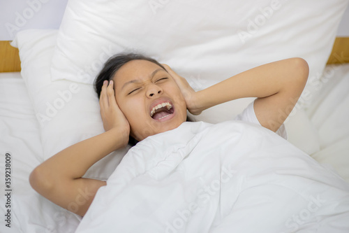 Emotional Stress And Overload. Asian Girl Shouting Covering Ears and laying In Bed At Home In The Morning.