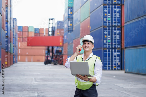 new normal concept, inspector engineer using laptop and walkie talkie for remote commanding in the factory or Container yard or check the correctness of the container before importing or exporting