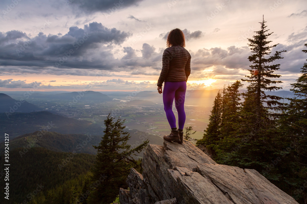Adventurous Girl on top of a Rocky Mountain overlooking the beautiful Canadian Nature Landscape during a dramatic Sunset. Taken in Chilliwack, East of Vancouver, British Columbia, Canada. Adventurous Girl on top of a Rocky Mountain overlooking the beautiful Canadian Nature Landscape during a dramatic Sunset. Taken in Chilliwack, East of Vancouver, British Columbia, Canada.