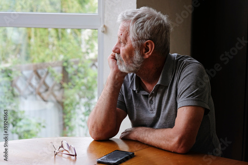 Senior retired man sitting at home alone while quarantine photo