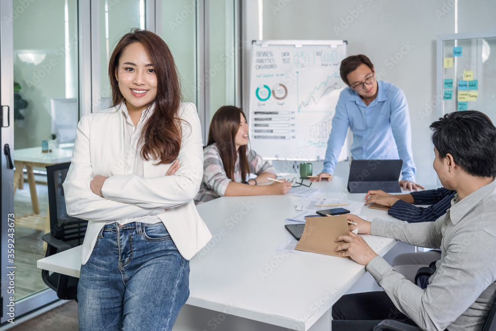 Portrait of Asian Business woman with Arms Crossed and standing over the group of colleague partner when brainstorming meeting at modern workplace, human resource and small business owner concept