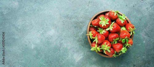 Fresh juicy strawberries in a bowl on a gray-green background, border. Top view, copy space, banner.