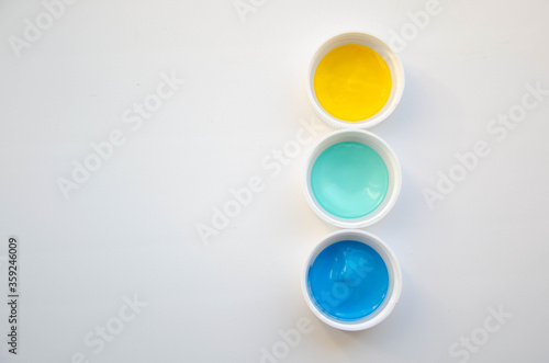 Three cups with yellow, mint and blue acrylic paint on the white background