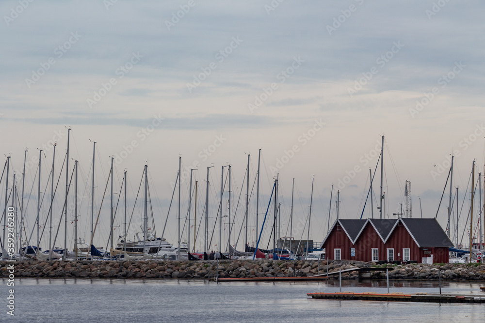 Sailboats marina with small dark red houses in fisherman's village.