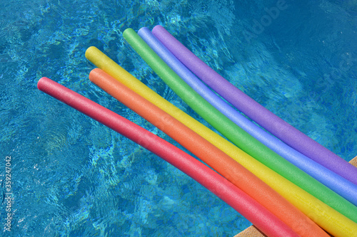 Rainbow coloured pool noodles floating in a swimming pool on a bright and sunny day