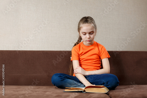 Child girl reading a book relaxing on a couch. Kids read books at home. Children learning and doing homework after school. Charming child on a sofa.