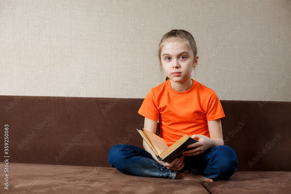 Caucasian Little Girl Sitting On The Sofa Reading a Book At Home Caucasian Little Girl Sitting On The Sofa Reading a Book At Home