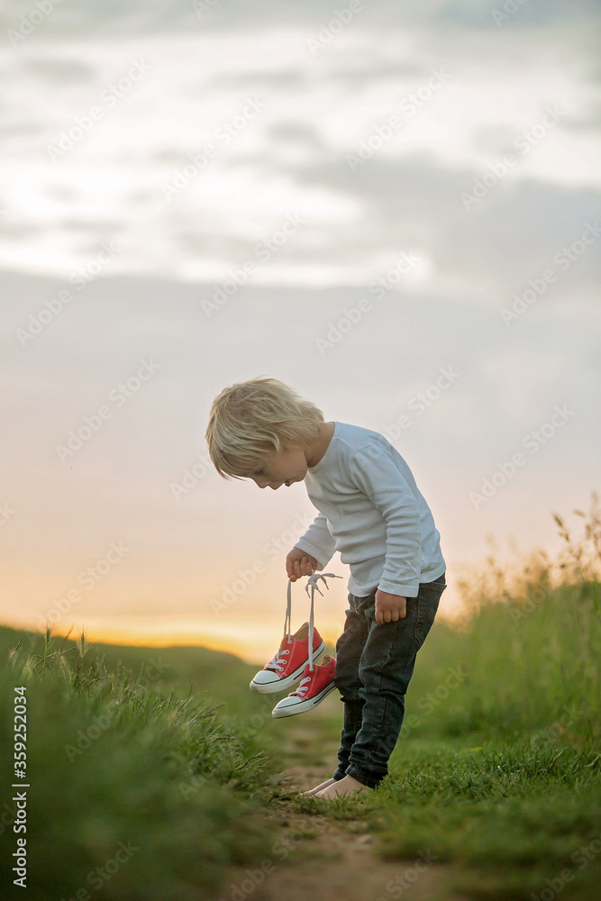 Happy child, holding pair of sneakers in hands, walking on a rural path Happy child, holding pair of sneakers in hands, walking on a rural path