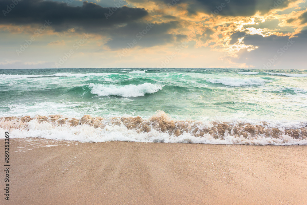 storm on the sandy beach at sunset. dramatic ocean scenery with cloudy sky. rough water and crashing waves in evening light