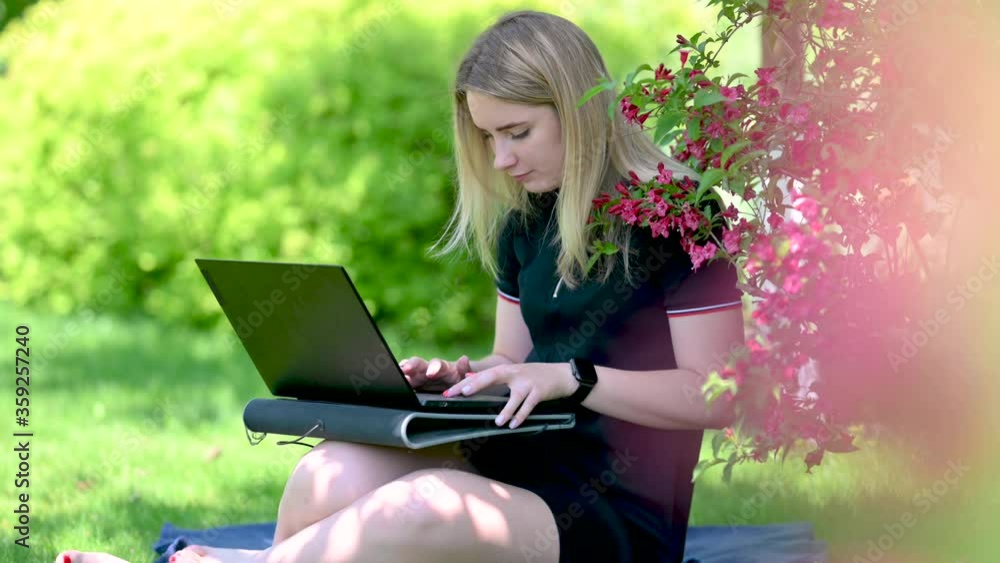 Girl working on a laptop while sitting on the grass in the park. work of the freelancer or blogger outdoors. Girl working on a laptop while sitting on the grass in the park. work of the freelancer or blogger outdoors.