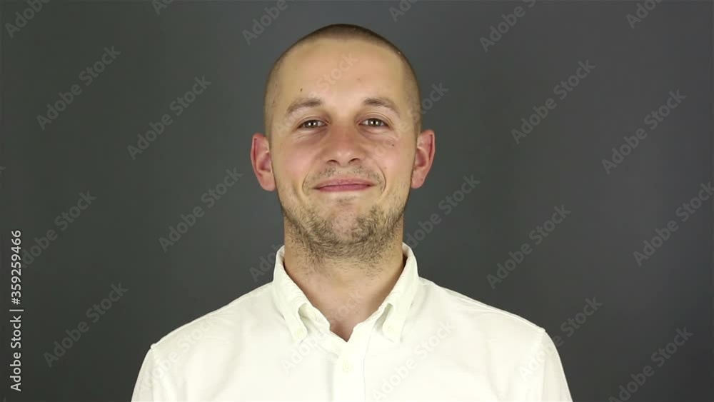 Young handsome guy in a white shirt, says goodbye and waves his hand. Portrait on a gray background. Young handsome guy in a white shirt, says goodbye and waves his hand. Portrait on a gray background.