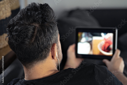 man hand holding using digital tablet watching online cooking master class using headphones. learning cooking remotely