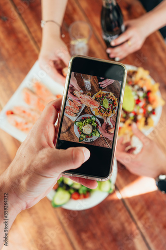 Vertical photo of last generation mobile taking a photo of the food that is on a wooden table with friends sharing the food
