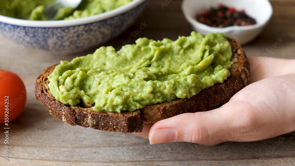 Rye bread toast with mashed avocado. Healthy vegan vegetarian breakfast or snack food. Avocado toast in hand Rye bread toast with mashed avocado. Healthy vegan vegetarian breakfast or snack food. Avocado toast in hand