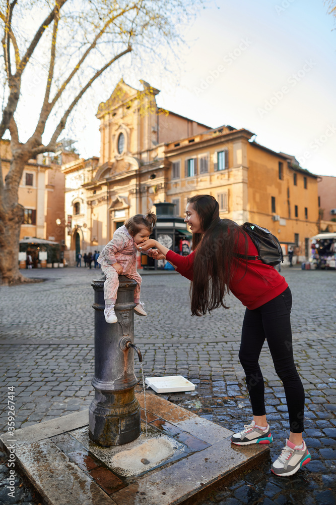 a mother gives her daughter a drink of water in a square in Rome