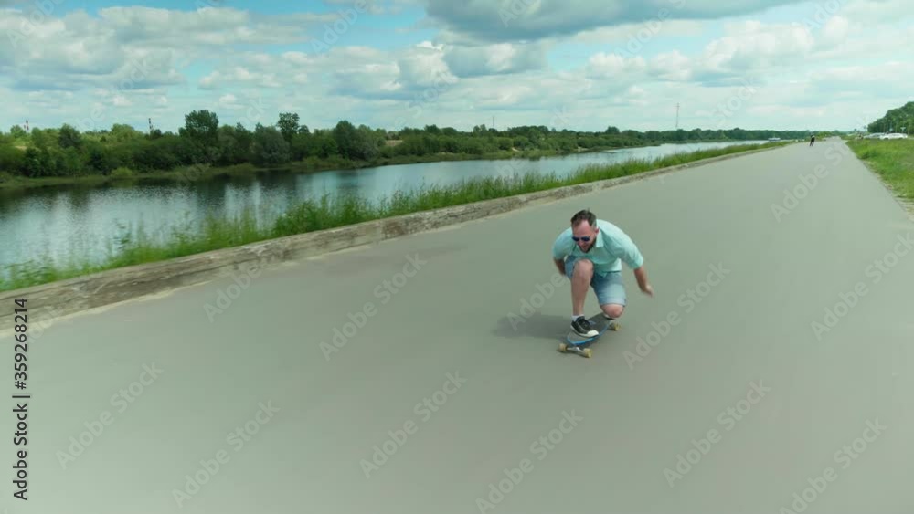 Young handsome man without a medical mask riding a skateboard on a road near a river, fooling around and having fun. Outdoors workout. High quality footage. N1H1 coronavirus quarantine. Young handsome man without a medical mask riding a skateboard on a road near a river, fooling around and having fun. Outdoors workout. High quality footage. N1H1 coronavirus quarantine.