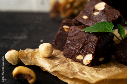 Fondant on craft crumpled paper with nuts and chocolate cubes decorated with green mint leaves. In the background a jar of nuts, blurred background. 