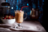 Ice coffee in a latte glass with cream poured over, ice cubes and beans on a gray towel. black background with copy space.