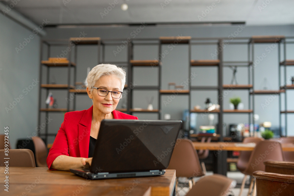 beautiful aged woman in a red jacket works in the office with a laptop beautiful aged woman in a red jacket works in the office with a laptop