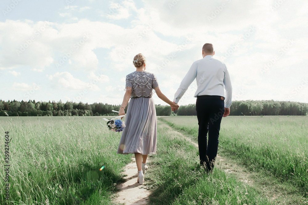 a young couple holding hands and holding a wedding bouquet in their hands goes across the green field into the distance