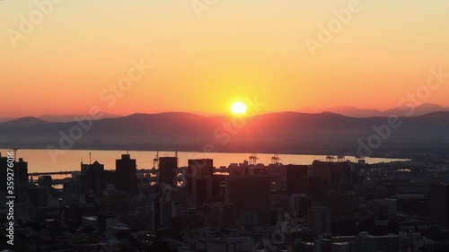 The sun rises over the city of Cape Town, South Africa. The harbour in Table Bay can be seen behind the city buildings.