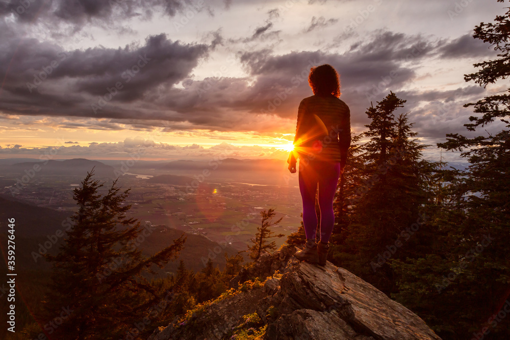 Fototapeta premium Adventurous Girl on top of a Rocky Mountain overlooking the beautiful Canadian Nature Landscape during a dramatic Sunset. Taken in Chilliwack, East of Vancouver, British Columbia, Canada.